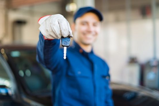 Image of a mechanic holding out a car key to the viewer.