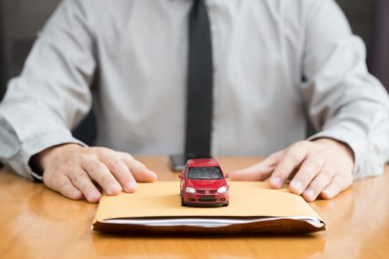 Image of a man with a tie sitting at a desk with a folder and a red toy car sitting on top of it.