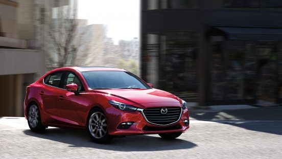Image of a red 2018 Mazda3 sedan driving on a city street.