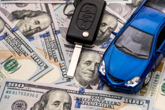 Image of a blue toy car and car keys sitting on $100 bills.