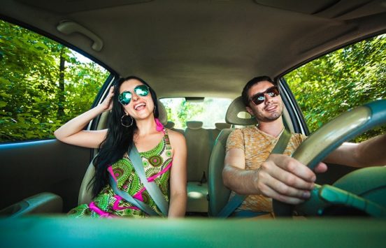 Image of a happy young couple driving in their car with sunglasses on.